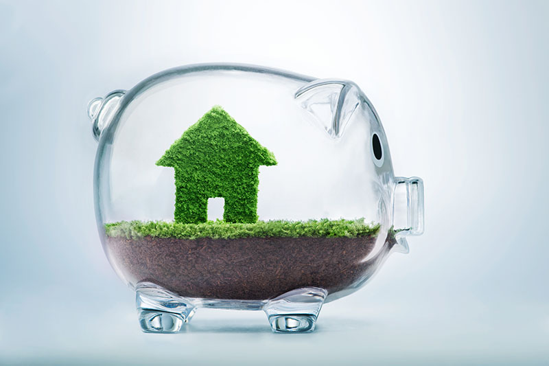 Learning Center 5 A transparent piggy bank contains soil and a small green house figure made of grass, symbolizing saving money for a home or eco-friendly housing investments.