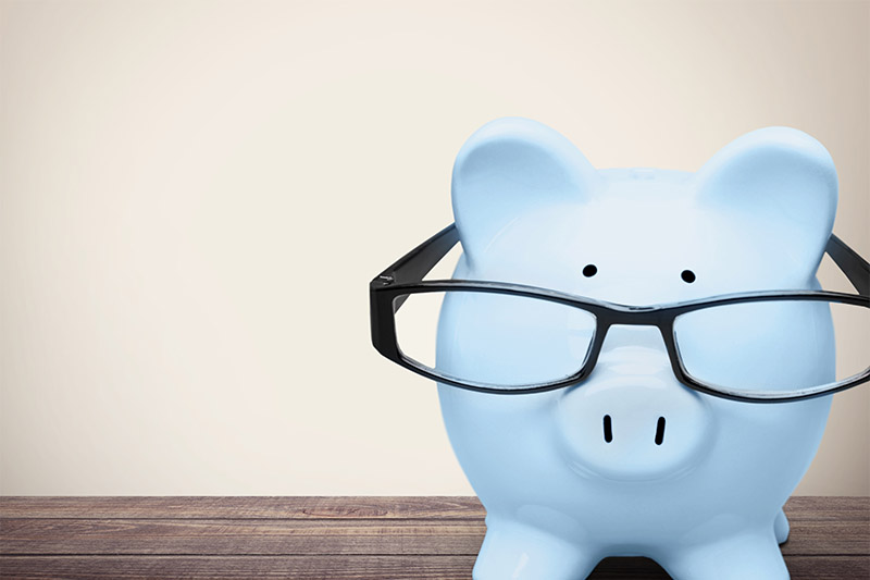 Learning Center 6 A light blue piggy bank wearing black eyeglasses sits on a wooden surface against a plain, beige background.