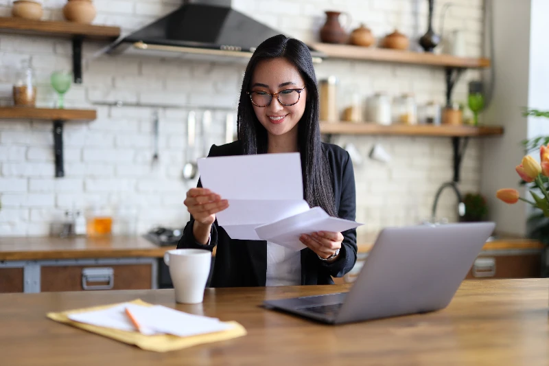 Businesswoman happily reads financial letter at a desk with laptop