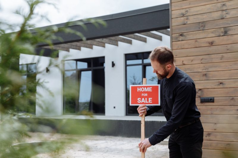 Man placing a home for sale sign outside a modern home